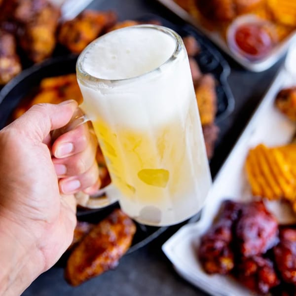 Hand holding a frosty mug of beer, surrounded by Goobne Chicken's fried chicken and waffle fries.