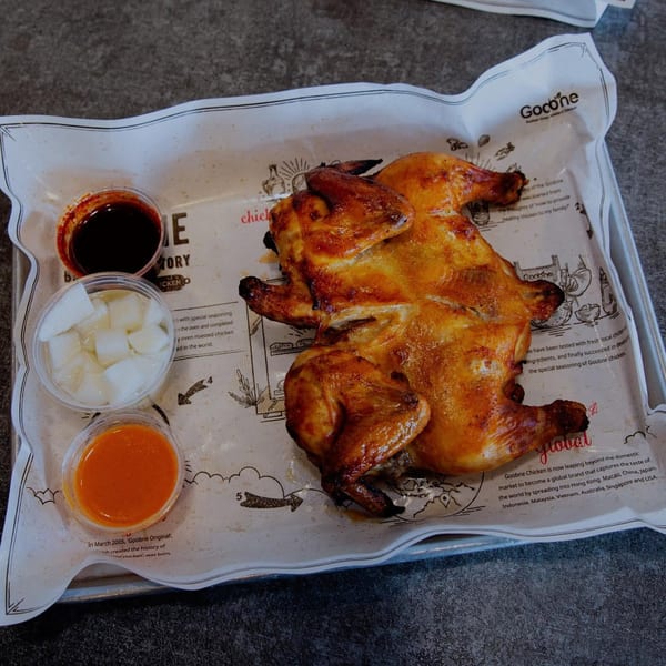 A whole roasted Goobne chicken with three dipping sauces on a branded paper-lined tray.