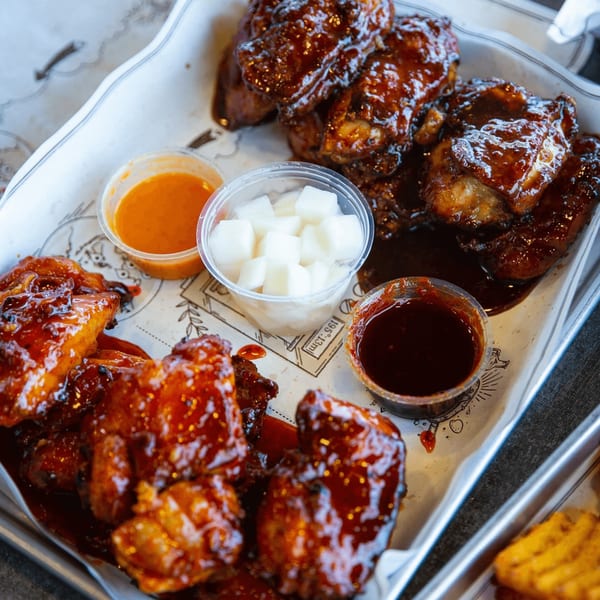 Goobne Chicken's glossy, sauced fried chicken pieces on a tray with dipping sauces and pickled radish.