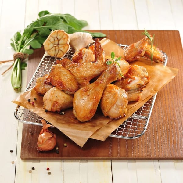 Goobne Chicken's roasted chicken pieces on a wire rack with garlic, herbs, and peppercorns.