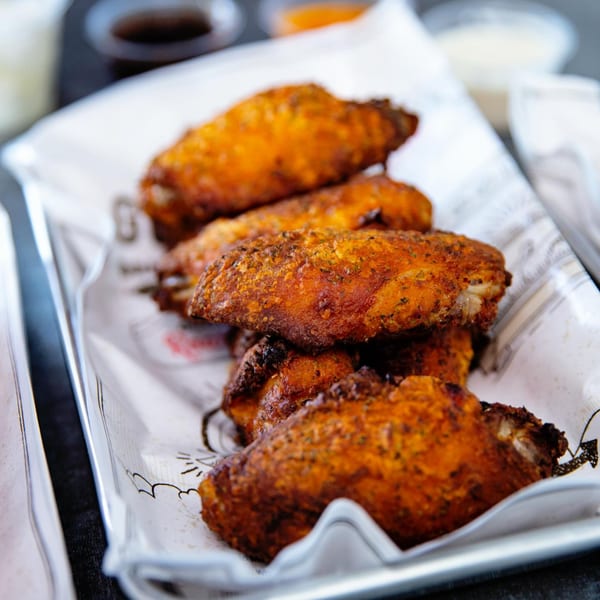 Close-up of crispy, golden-brown Goobne fried chicken wings on a white paper-lined tray.