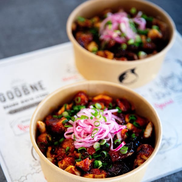 Two Goobne Chicken bowls filled with saucy chicken, topped with pickled red onions and green onions.