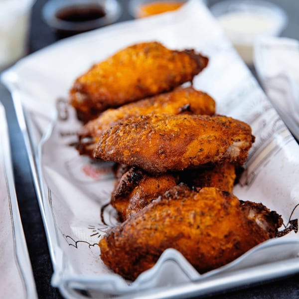 Close-up of crispy, golden-brown Goobne fried chicken wings on a white paper-lined tray.